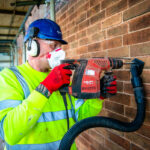 Man with protective clothing drilling into brick wall