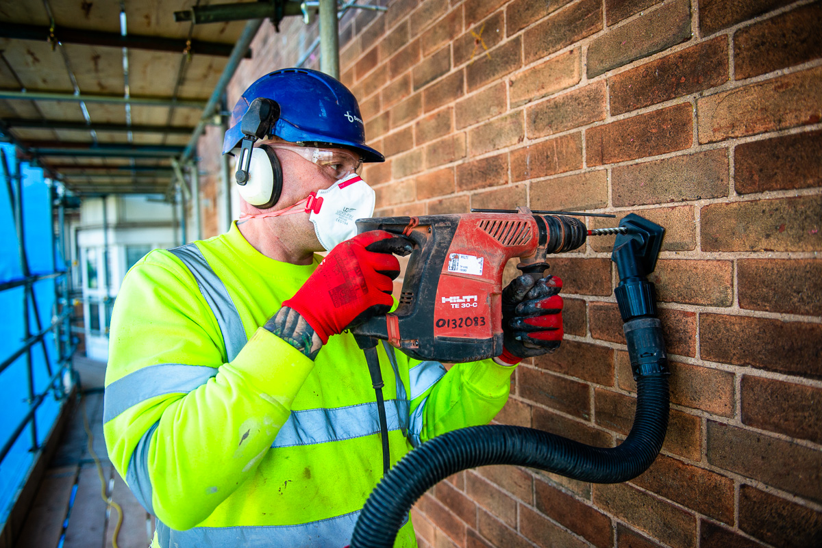 Man with protective clothing drilling into brick wall