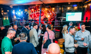Photo of busy event space with people chatting and band playing